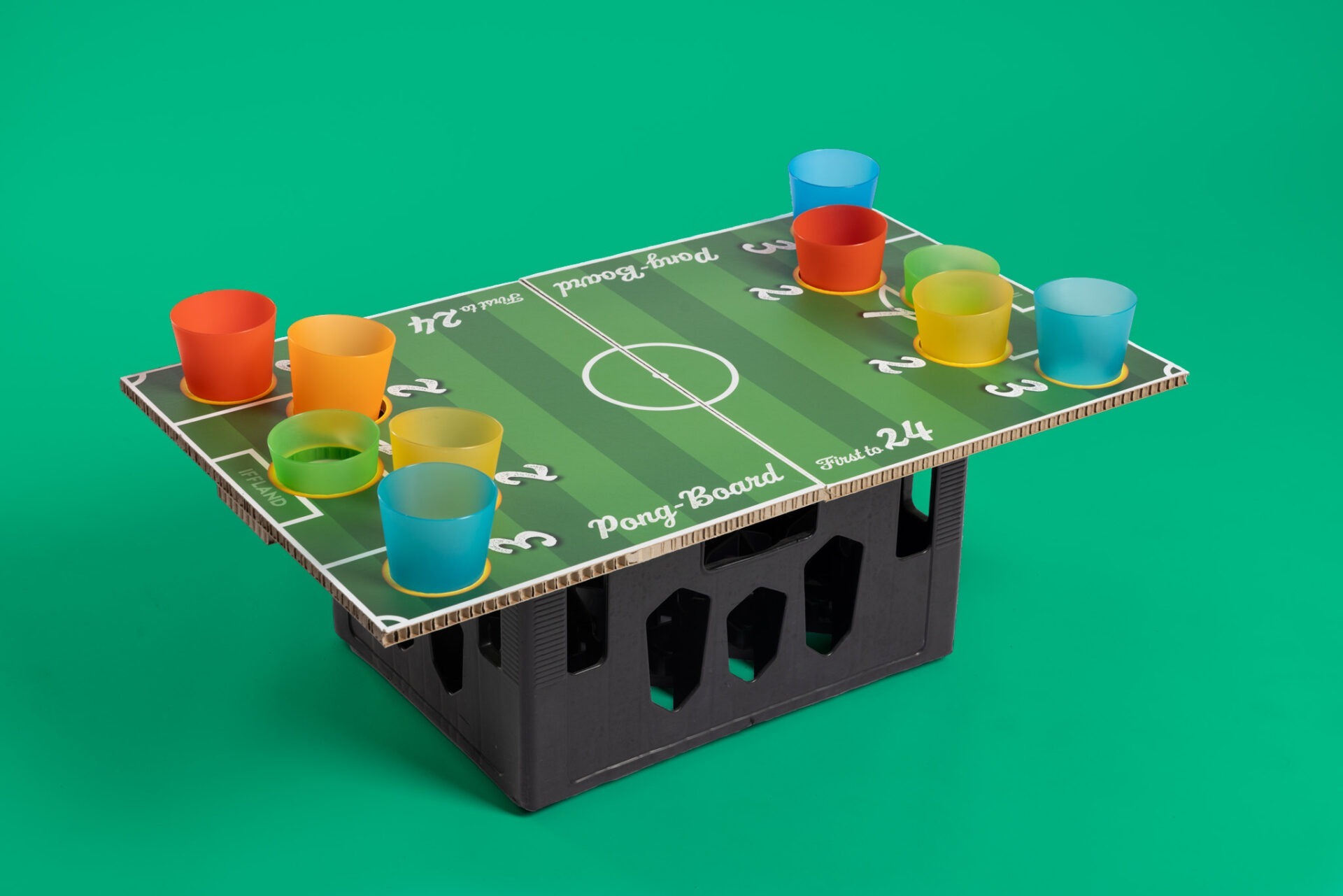 Pong-Board mit Fußballfeld-Design steht auf schwarzer Getränkekiste, bunte Becher auf markierten Punkten, gefertigt von IFFLAND.