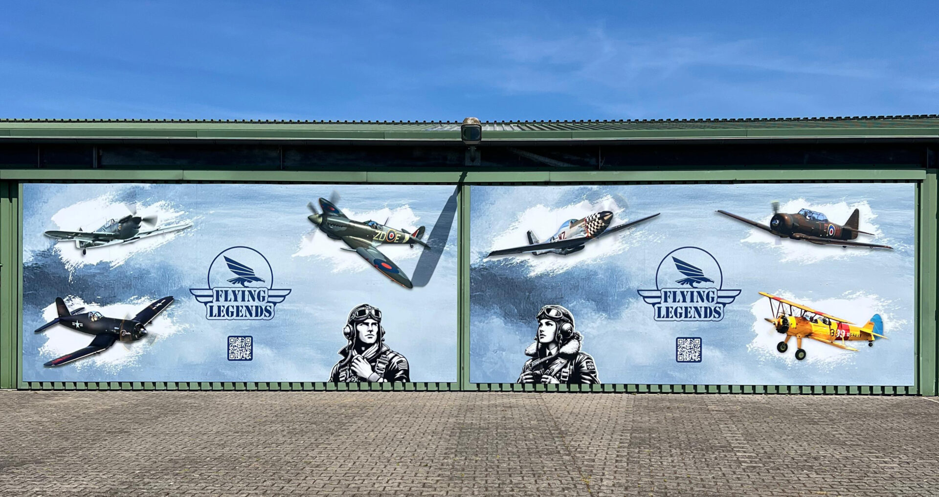 Große Hallenwand mit bedruckter Werbefläche für „Flying Legends“, zeigt historische Flugzeuge und Pilotenporträts, produziert von IFFLAND.