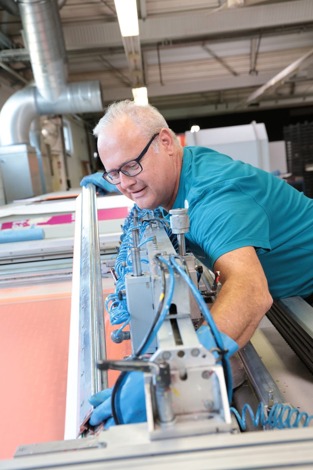 Foto aus der Druckabteilung: Ein IFFLAND Mitarbeiter mit Handschuhen steht an einer großen Siebdruckmaschine und bedient diese.