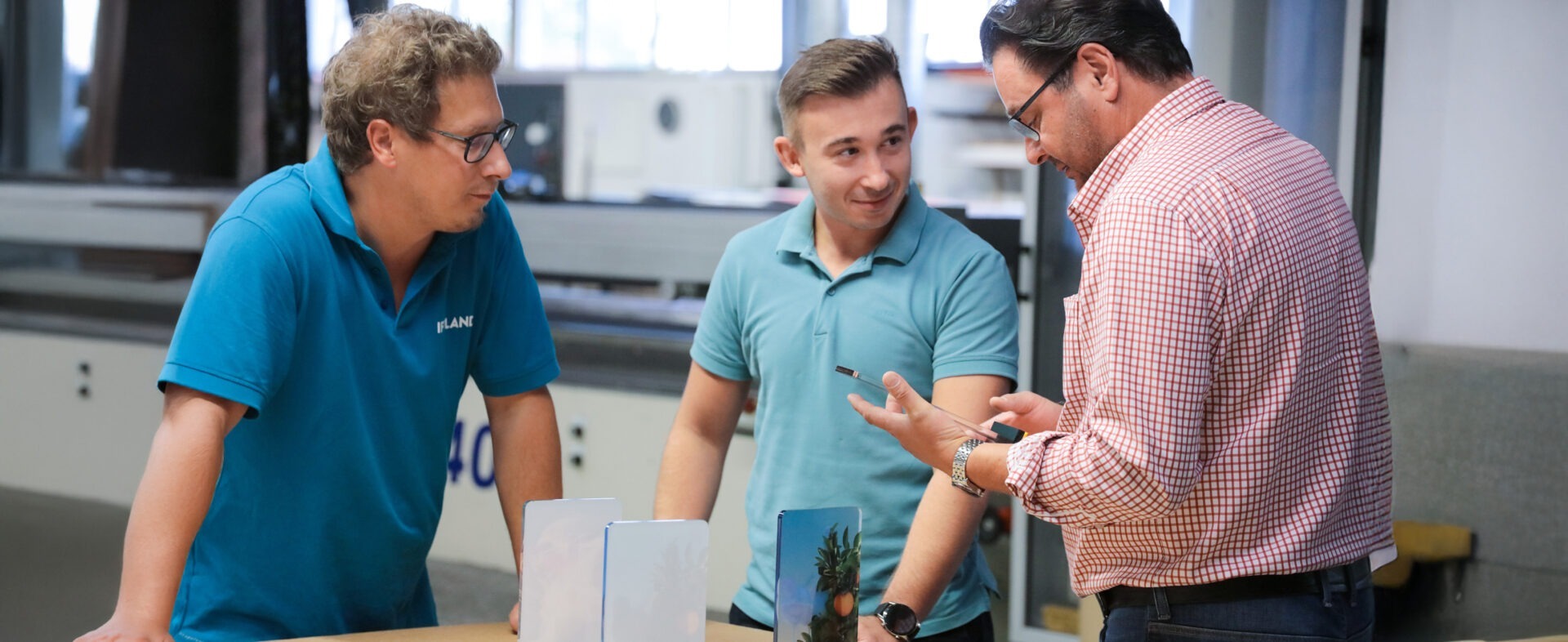 Drei sympathisch lächelnde Mitarbeiter von IFFLAND aus verschiedenen Abteilungen stehen zusammen um ein Kundenprodukt und machen Qualitätskontrolle.